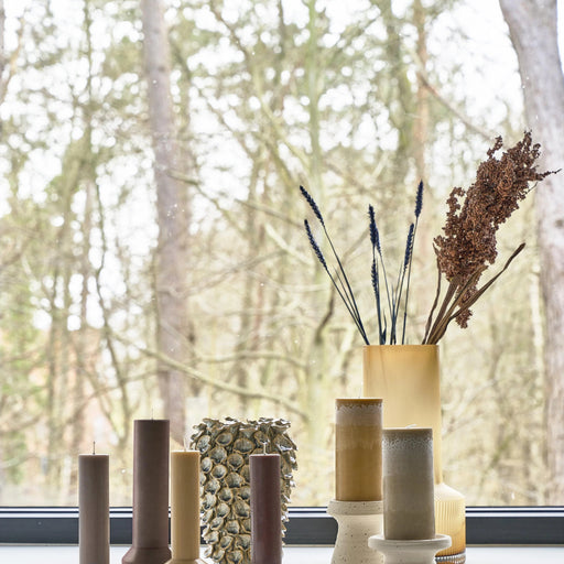 Decorative vases and candles on a windowsill with a blurred forest background