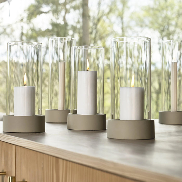 Set of pillar candles in glass holders on a wooden surface with a blurred natural background