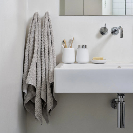 Bathroom with a sink, towel, and toiletries on a light gray wall.