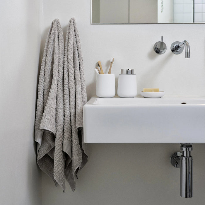Bathroom with a sink, towel, and toiletries on a light gray wall.