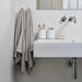 Bathroom with a sink, towel, and toiletries on a light gray wall.