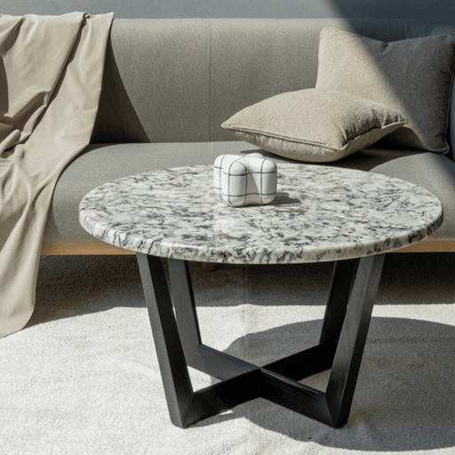 Round marble coffee table with black legs in front of a beige sofa.