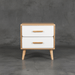 Wooden nightstand with two white drawers and wooden handles against a gray concrete wall.