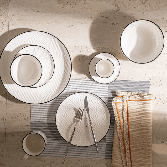 Dining table setting with white ceramic plates, cutlery, and a folded napkin on a textured surface.