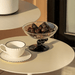 White teacup and saucer with a glass bowl containing dates on a beige table.