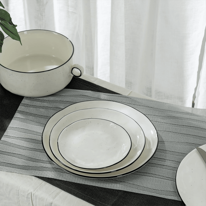 White ceramic plates with black rims on a gray placemat, with a white curtain in the background.