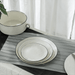 White ceramic plates with black rims on a gray placemat, with a white curtain in the background.