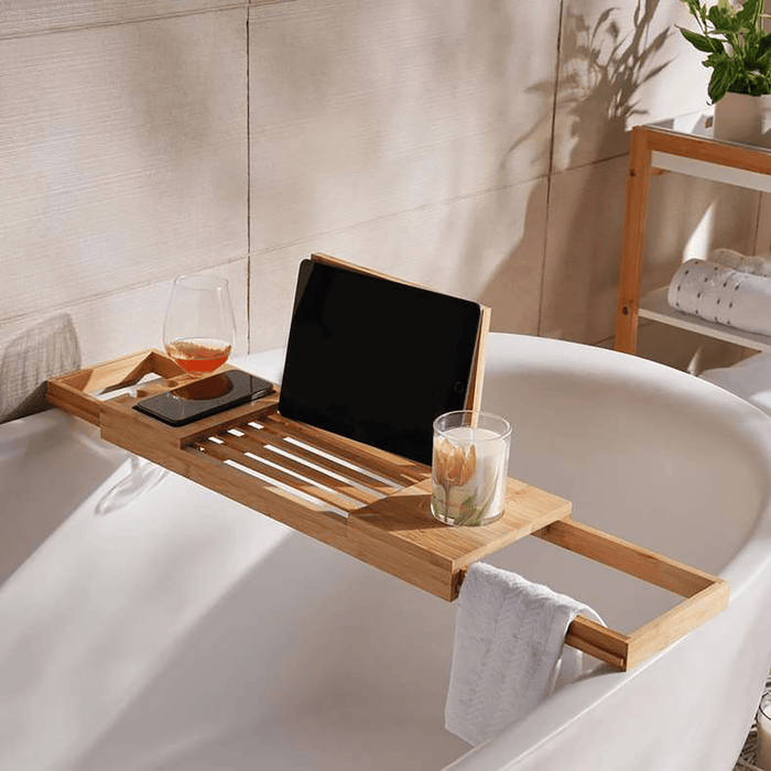 Wooden bathtub caddy with tablet, glass of wine, and candle in a bathroom setting.