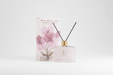 White diffuser bottle with packaging featuring floral design on a light gray background