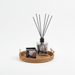 Diffuser with black sticks on a woven tray with a candle on a white background