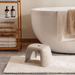 White stool in front of a bathtub with towels and bottles on a shelf in a bathroom setting.