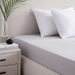 Bed with white bedding and pillows, nightstand with books and plant in the corner.