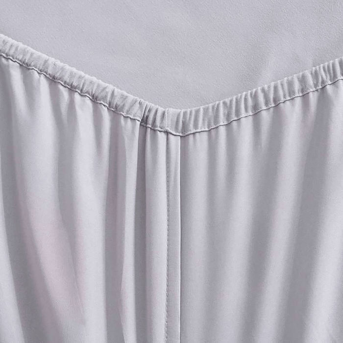 Close-up of a light gray fitted sheet on a bed with a plain background