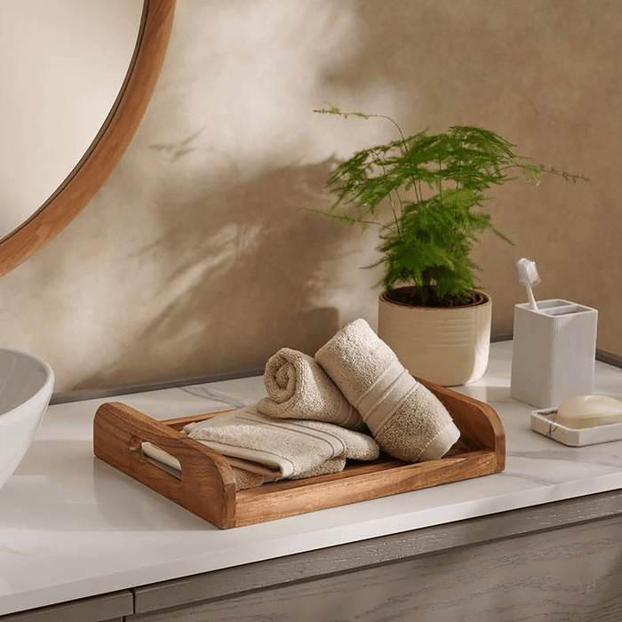 Bathroom counter with towels on a wooden tray, plant, and bathroom accessories.