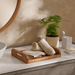 Bathroom counter with towels on a wooden tray, plant, and bathroom accessories.
