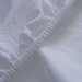 Close-up of white fitted sheet with subtle texture and stitching details.