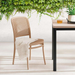 Wicker chair with a white cloth draped over it next to a wooden table with a glass of water, against a white wall with greenery.
