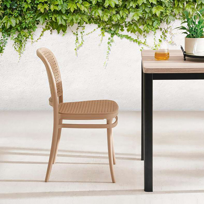 Wooden chair and table with a white wall and greenery in the background