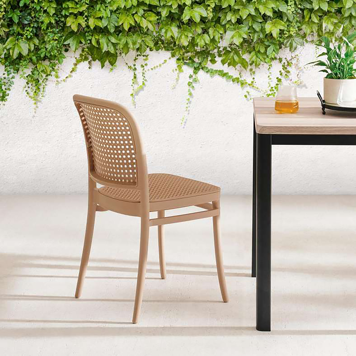 Beige wicker chair next to a black table with a white wall and greenery in the background