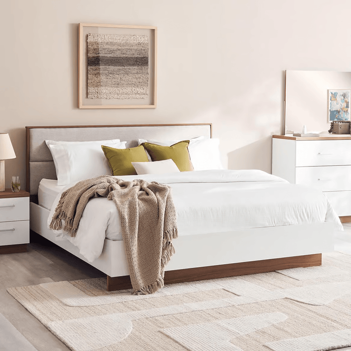 Neatly made bed with white bedding and decorative pillows in a bedroom setting.