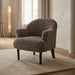 A single upholstered accent chair with a textured, speckled taupe-brown fabric and dark turned wooden legs, set on a cream rug in a softly lit living room.