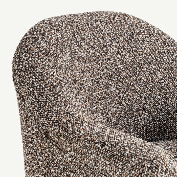 Close-up of a textured upholstered armchair showing the fabric weave in a speckled brown, beige, and white pattern against a light off-white background.