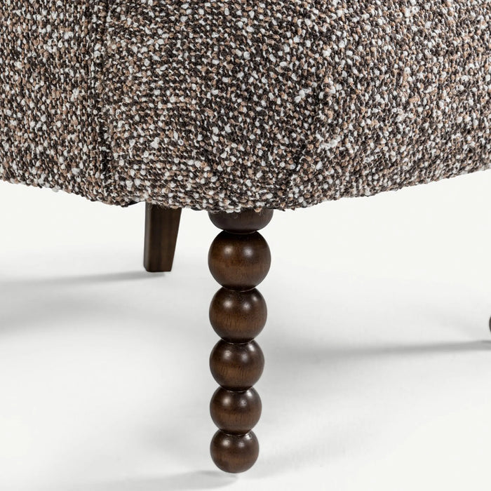 Close-up of a textured brown and beige upholstered furniture piece with a dark brown beaded wooden leg on a white background.