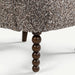 Close-up of a textured brown and beige upholstered furniture piece with a dark brown beaded wooden leg on a white background.