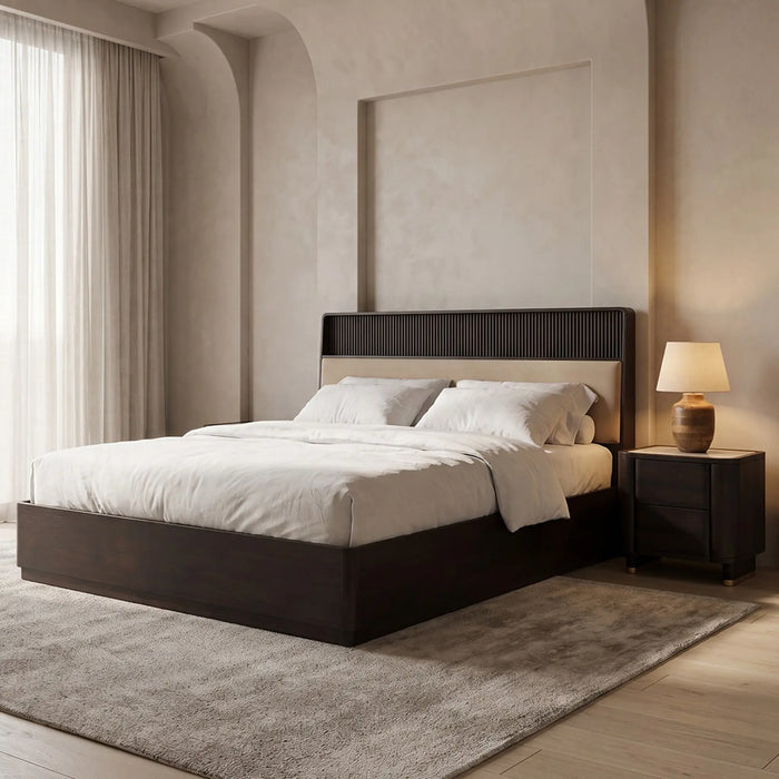 A modern platform bed with a dark wood frame and a ribbed headboard, dressed in white bedding, set in a minimalist bedroom with a matching nightstand, textured rug, and warm ambient lighting.