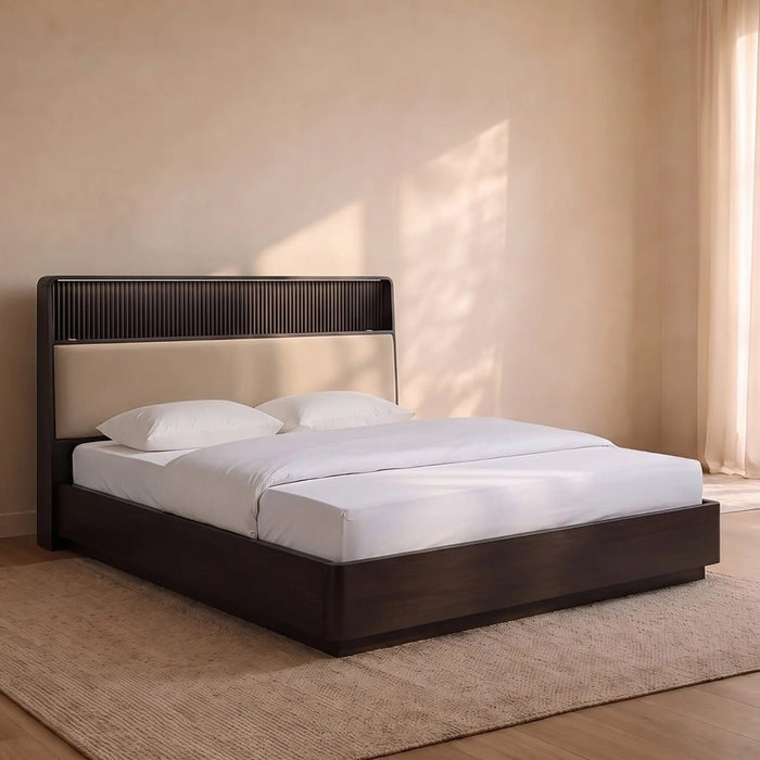 A modern platform bed with a dark wood frame and a beige upholstered headboard, styled with white bedding and pillows in a warm, minimalist bedroom setting.