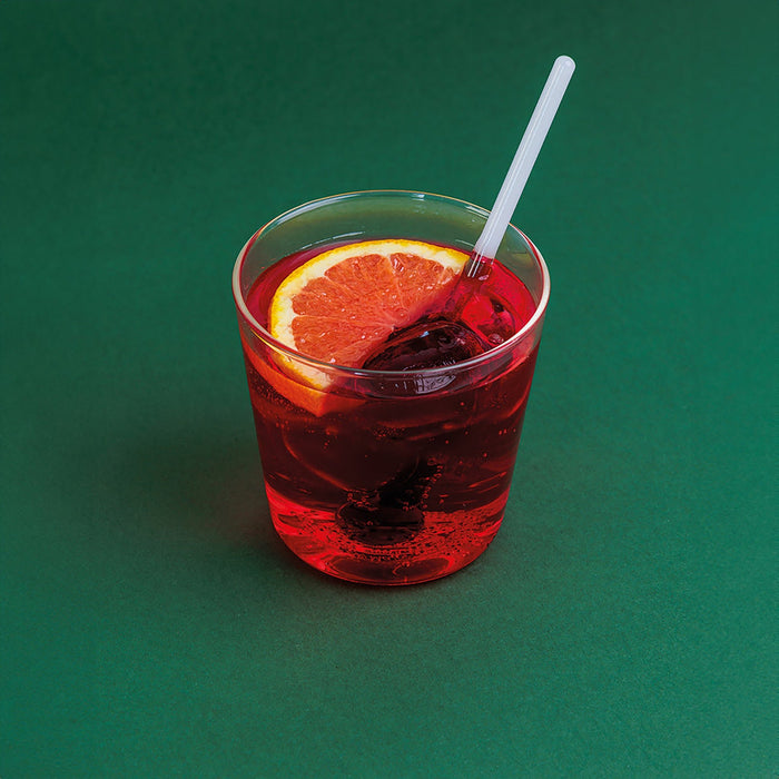 Red cocktail with an orange slice and a straw on a green background