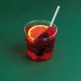 Red cocktail with an orange slice and a straw on a green background