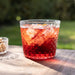 Red cocktail with ice in a glass on a wooden table outdoors