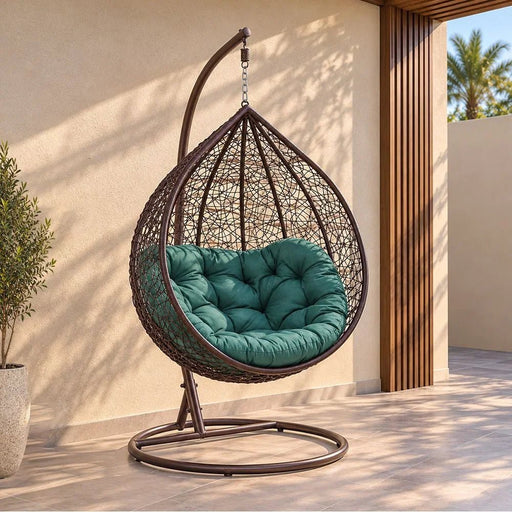 Teardrop-shaped woven outdoor hanging chair with a tufted teal cushion, suspended from a dark metal frame on a patio against a beige wall.