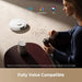Woman using a coffee grinder with a robot vacuum cleaner on a table, featuring voice compatibility with Alexa, Google Home, and Siri.