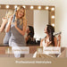 Two women using hair styling tools in front of a mirror with lights.