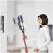 Woman holding a Dyson vacuum cleaner next to a wall-mounted dock.