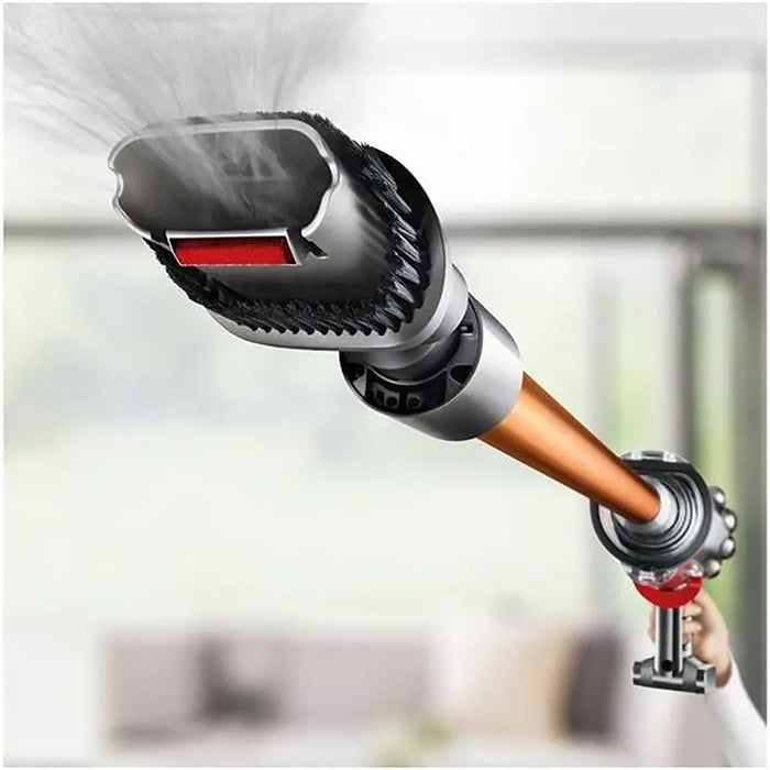 Handheld cleaning tool with a hose and nozzle, spraying water against a blurred indoor background.