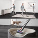 Person using a cordless vacuum cleaner in a room with a dog walking by.
