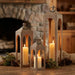 Wooden lanterns with candles on a wooden surface in front of a fireplace.
