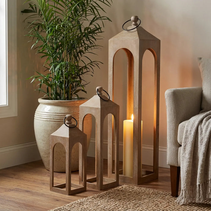 Decorative wooden lanterns with a candle and a potted plant in a room setting.