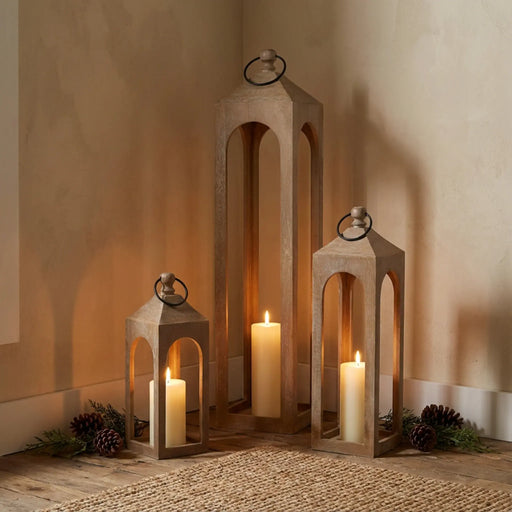 Wooden lanterns with candles on a wooden floor against a beige wall