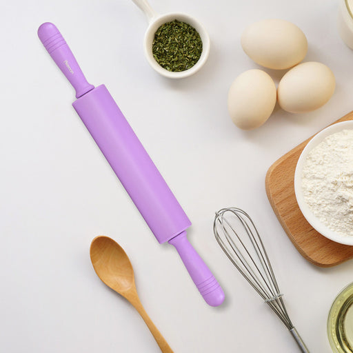 Purple rolling pin on a kitchen counter with eggs, flour, and a whisk.