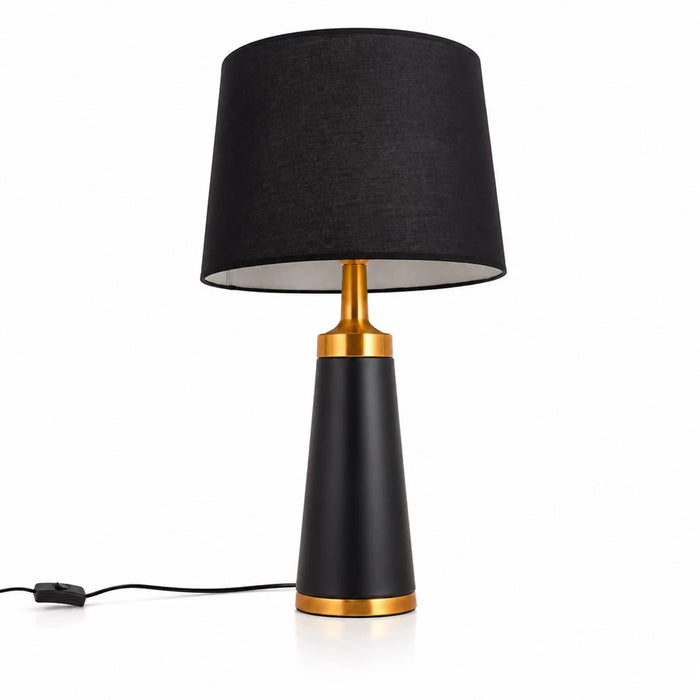 A modern table lamp with a black fabric drum shade, a matte black tapered base, and polished gold metal accents at the neck and bottom, shown on a white background with its power cord visible.