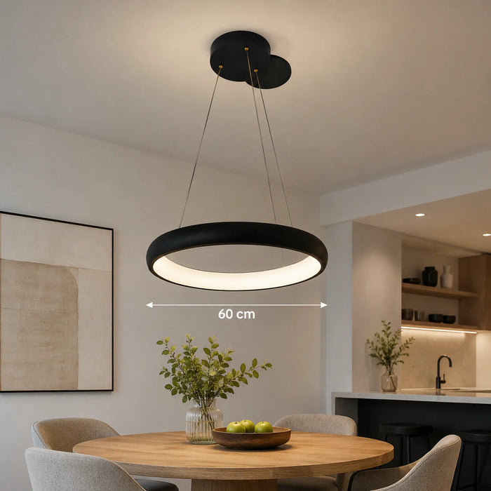 A modern black circular pendant light with a glowing white LED ring, suspended from a cloud-style ceiling canopy in a dining room. A white dimension overlay indicates the light's width is 60 cm.