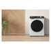 White washing machine with black door on a wooden floor against a beige wall with a geometric wood panel.