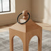Wooden stool with a black ring on top in a room with a window and rug.