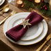 Christmas table setting with gold cutlery, white plates, red napkins, and star decorations on a wooden table.