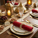 Decorative table setting with gold lanterns, candles, and red napkins on a wooden table.