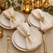 Elegant table setting with gold napkin rings, plates, and cutlery on a beige tablecloth.